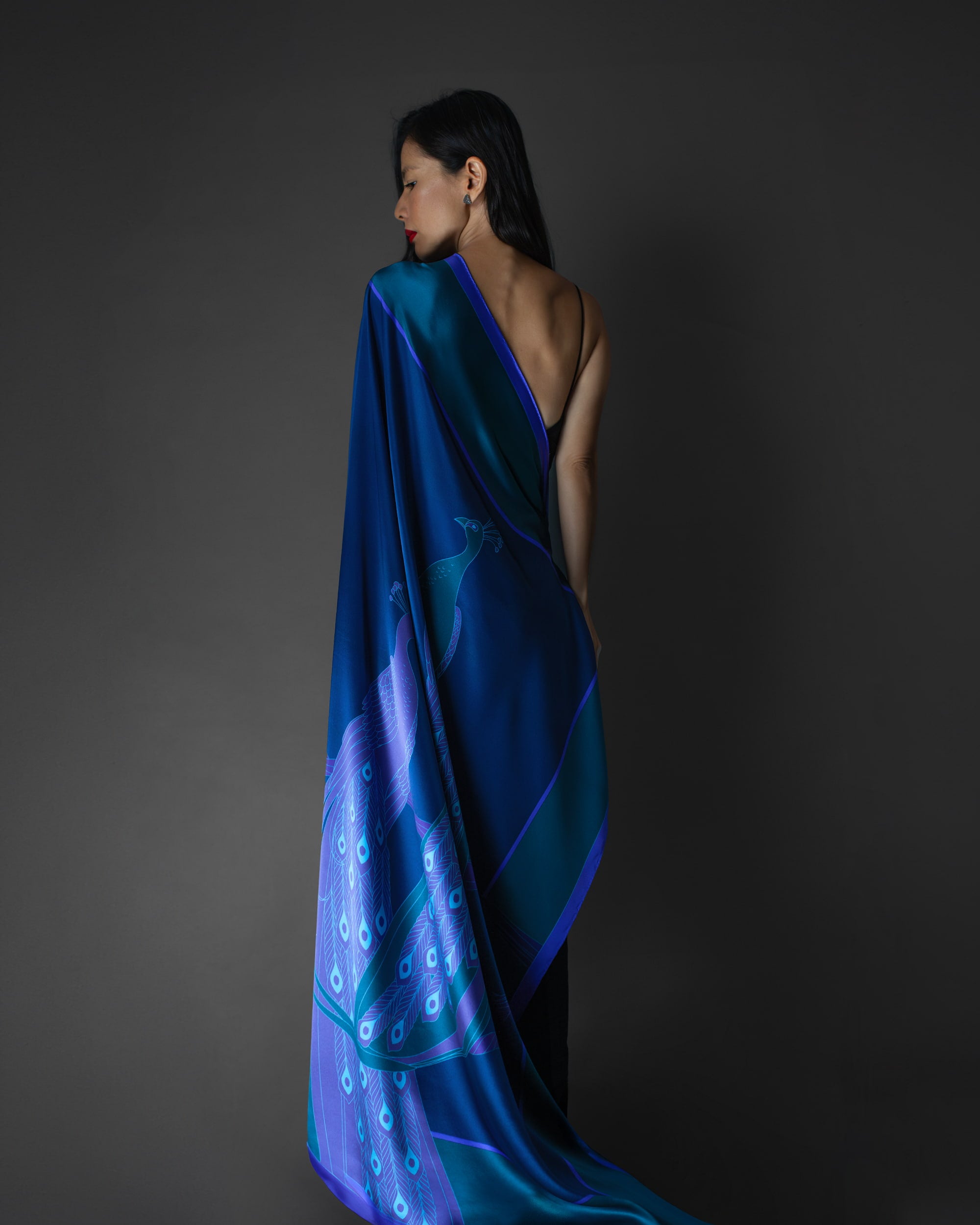 An asian model draped in a dark sapphire blue silk foulard with peacock feather patterns