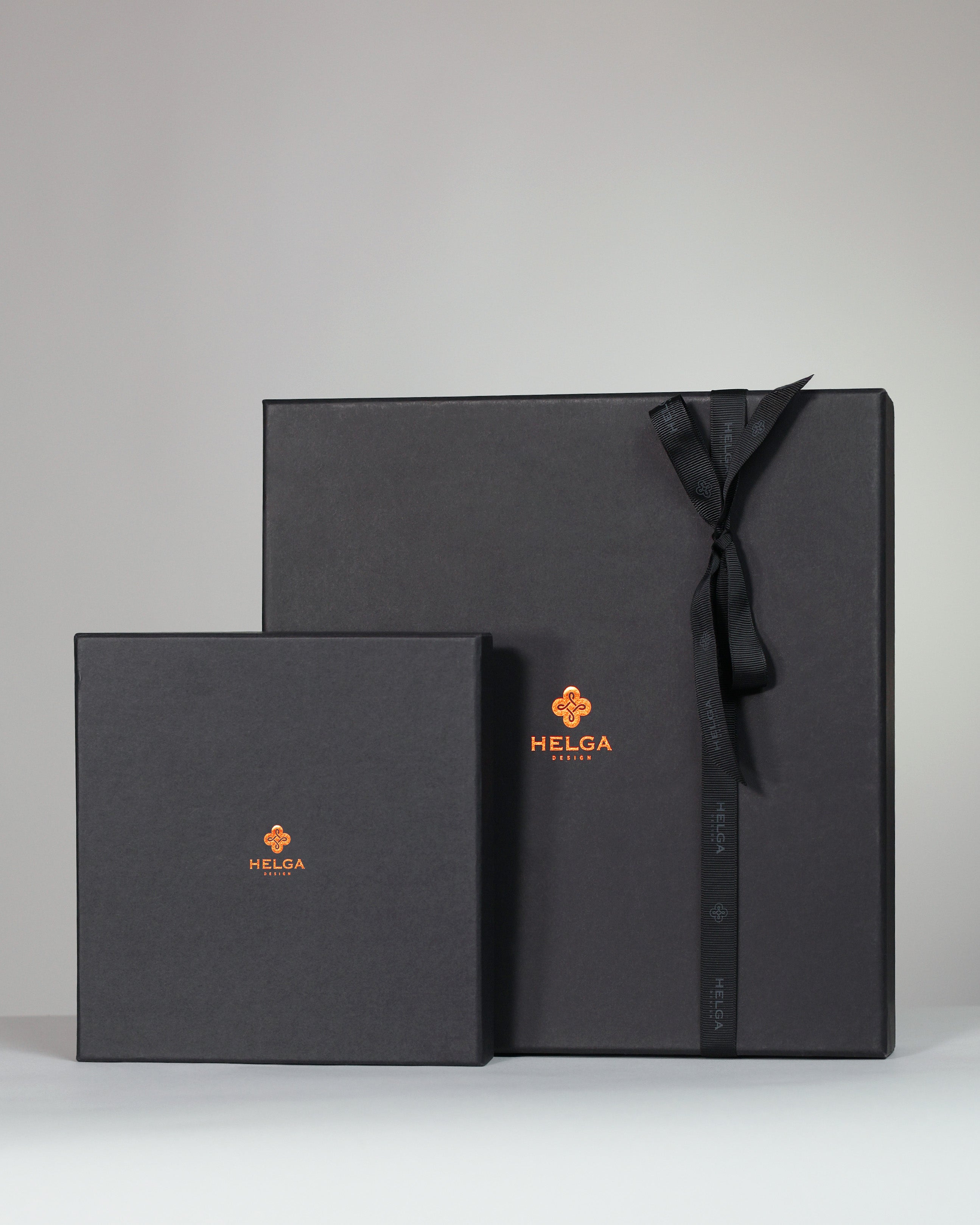Two black gift boxes with a bow, featuring the HELGA DESIGN brand logo, on a light gray background.