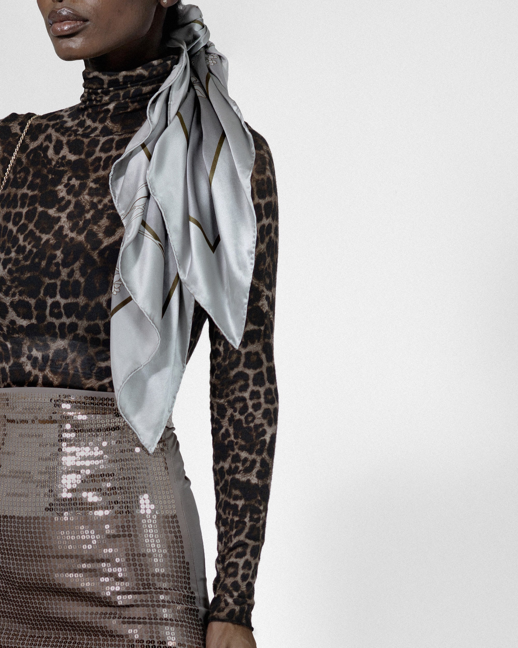Person wearing a leopard print top and gray skirt with a light gray silk scarf on a white background