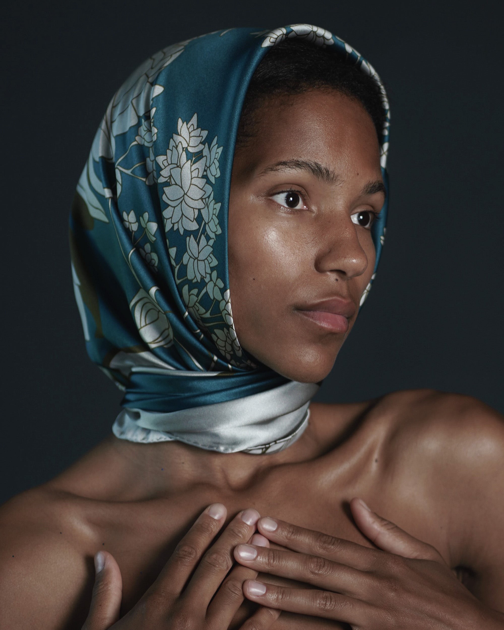 Woman wearing a patterned headscarf against a dark background