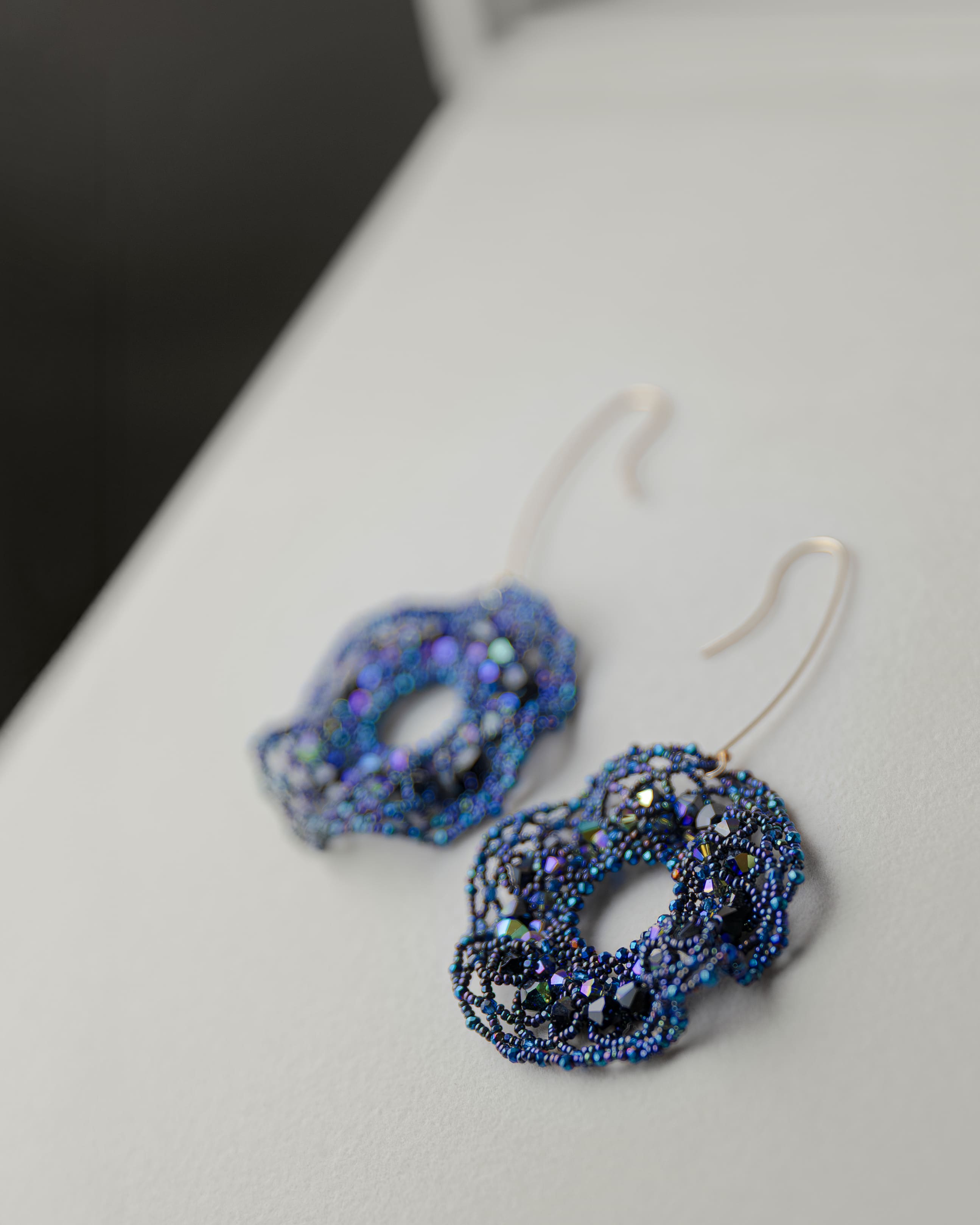 Blue beaded earrings on a white surface with a dark background