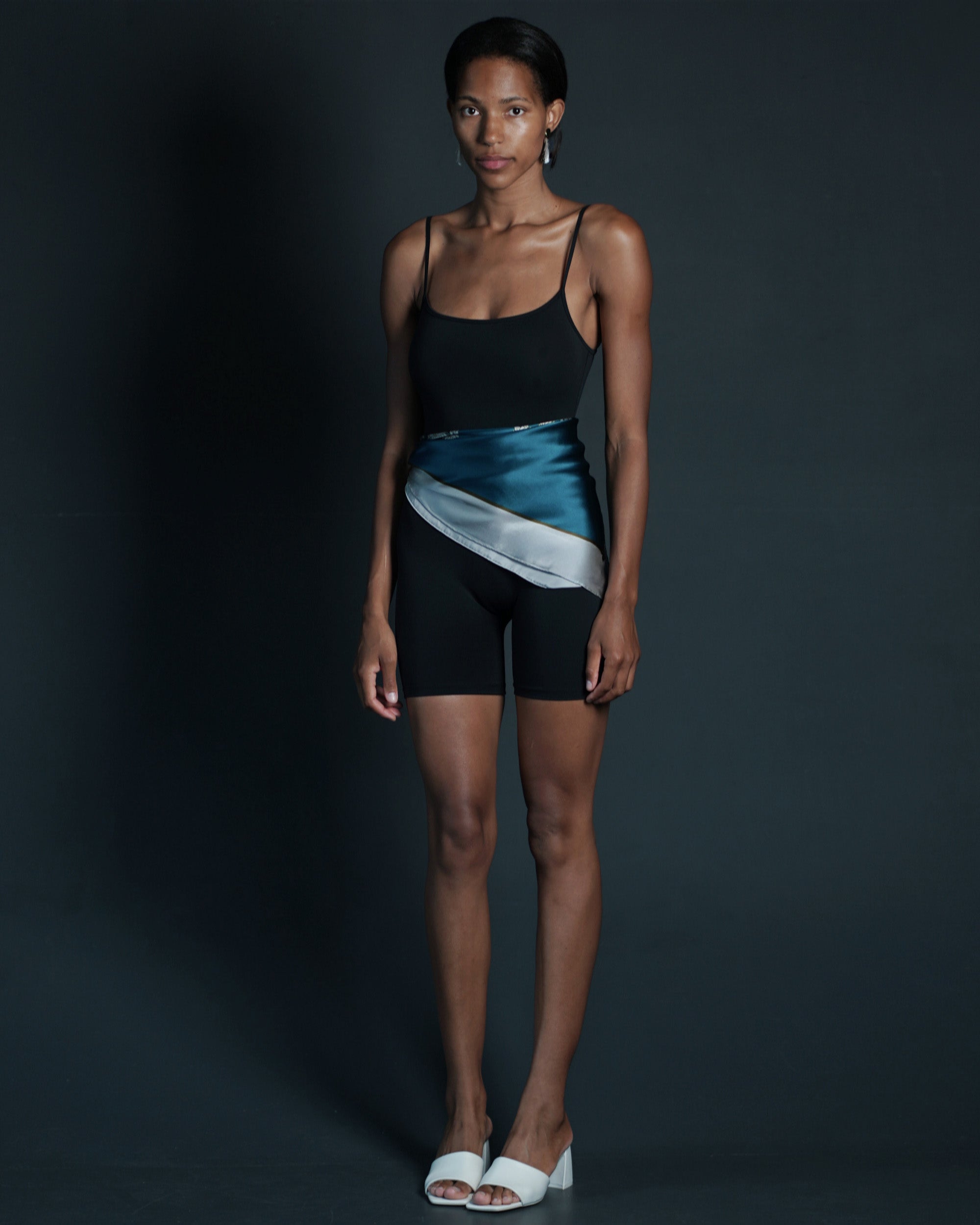 Model wearing HELGA-DESIGN teal green floral silk scarf wrapped around waist in combination with sport jumpsuit