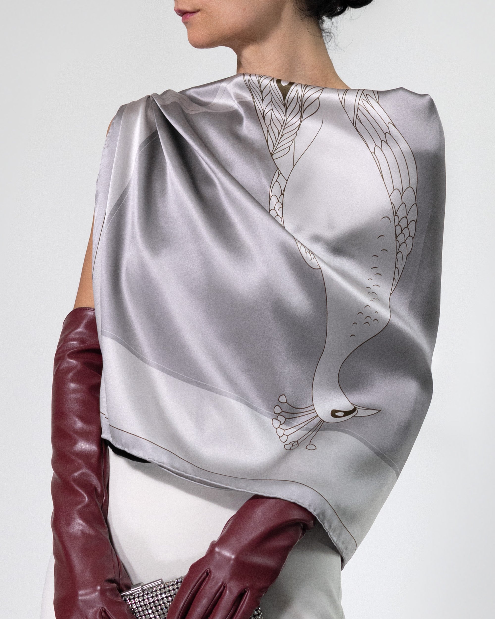 Silver scarf with intricate design worn by a person, paired with maroon gloves on a white background