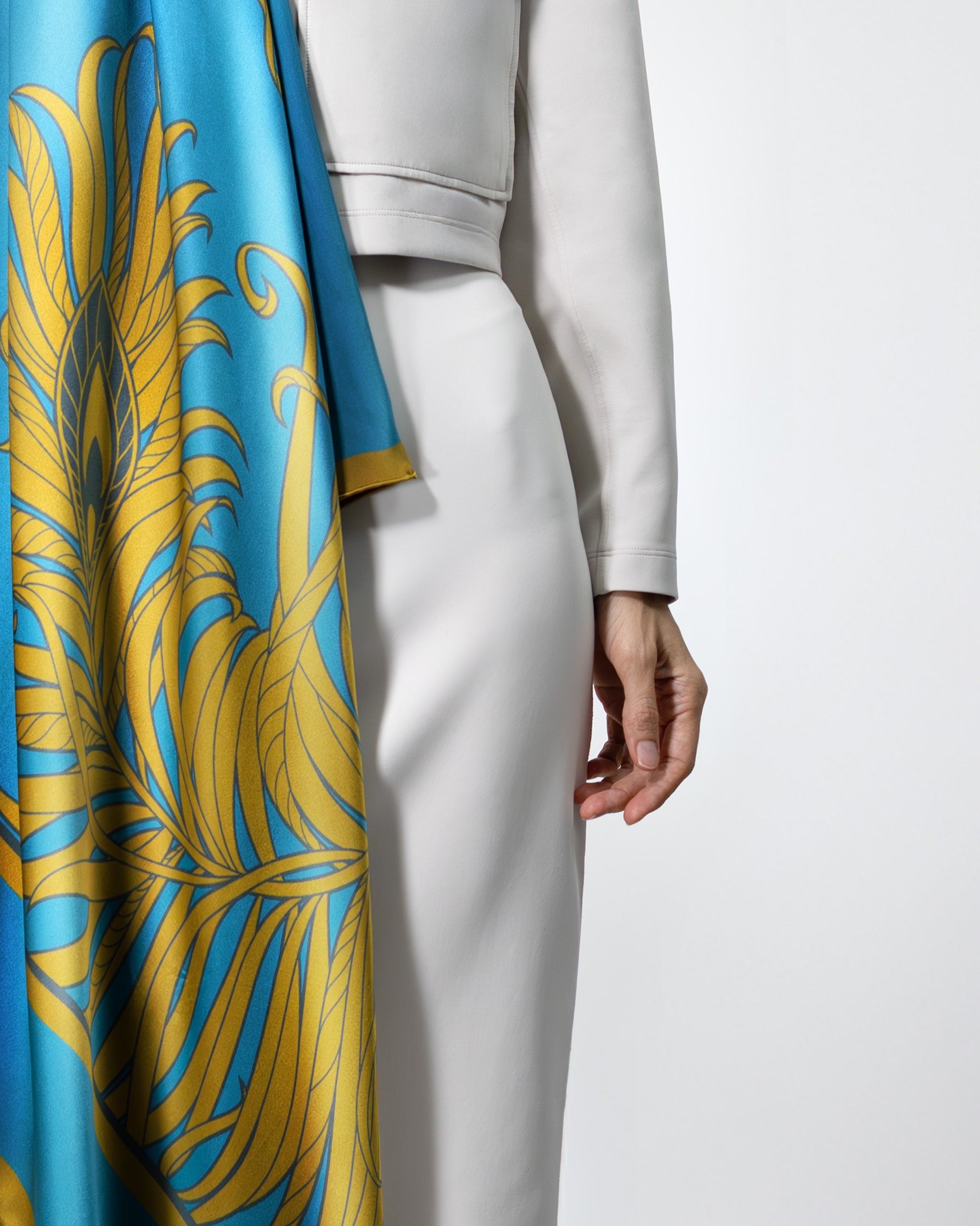 Person wearing a white outfit with a blue and gold patterned fabric draped over one shoulder.
