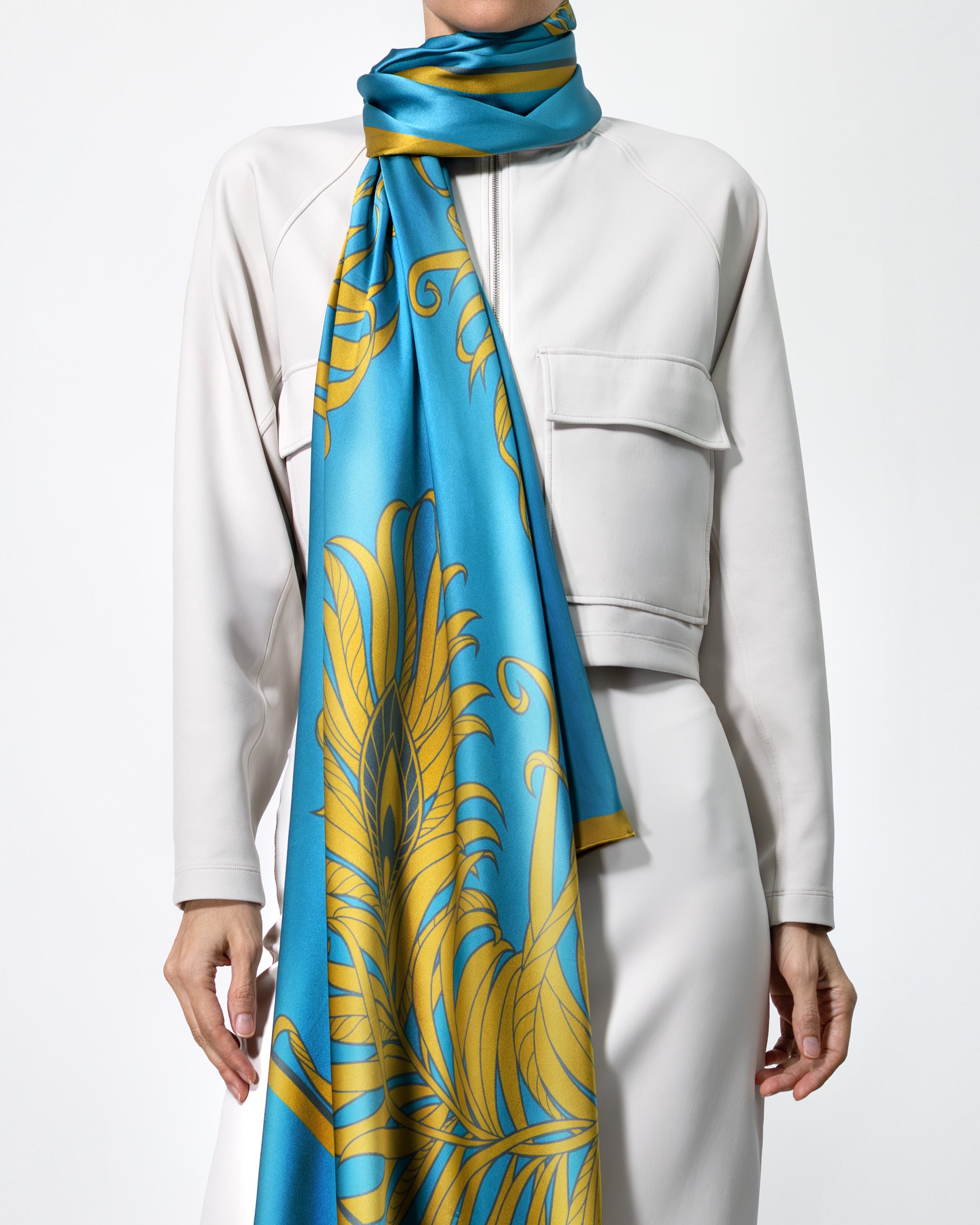 Person wearing a blue and gold patterned scarf with a white outfit on a light gray background