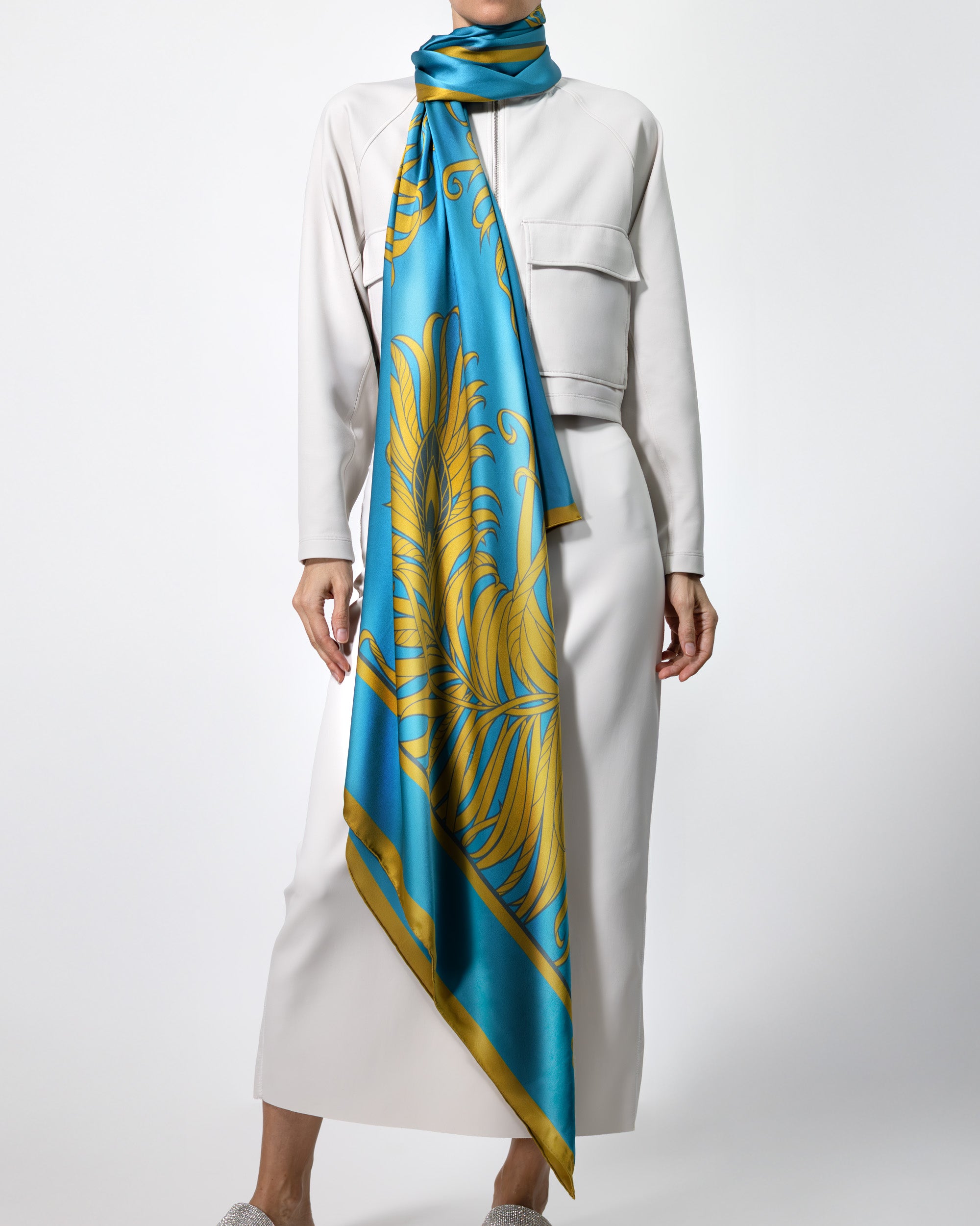 Person wearing a white outfit with a blue and gold patterned scarf on a white background